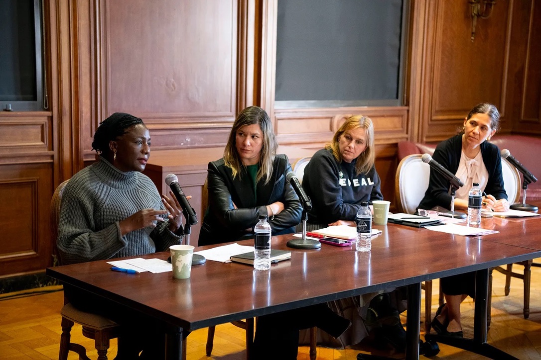 four women sitting at a table, one is talking and the other three are listening